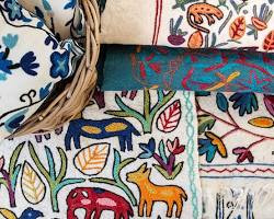Traditional Kashmiri Namda felted wool floor covering with colourful designs alongside vibrant Crewel work embroidery on durable fabric.